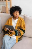 African american girl holding digital tablet touch screen typing scroll page at home. Woman with mobile tech device surfing internet using social media apps playing game. Study work shopping online. photo