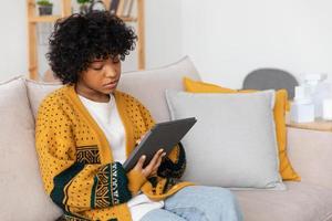 African american girl holding digital tablet touch screen typing scroll page at home. Woman with mobile tech device surfing internet using social media apps playing game. Study work shopping online. photo