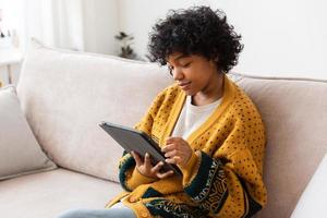 African american girl holding digital tablet touch screen typing scroll page at home. Woman with mobile tech device surfing internet using social media apps playing game. Study work shopping online. photo