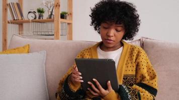 African american girl holding digital tablet touch screen typing scroll page at home. Woman with mobile tech device surfing internet using social media apps playing game. Study work shopping online. photo