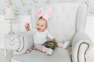 Little child girl wearing bunny ears on Easter day and playing with painted eggs photo