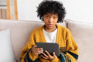 African american girl holding digital tablet touch screen typing scroll page at home. Woman with mobile tech device surfing internet using social media apps playing game. Study work shopping online. photo
