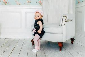 Little baby girl standing near chair in bright light living room smiling and laughing photo