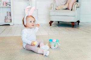 Little child girl wearing bunny ears on Easter day and playing with painted eggs photo