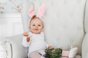 Little child girl wearing bunny ears on Easter day and playing with painted eggs photo