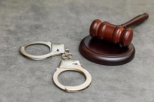 Law theme. Court of law trial in session. Judge gavel handcuffs on grey table in lawyer office or court session. Mallet of judge on concrete stone grey background. Justice human rights concept. photo