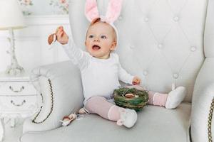 niña pequeña con orejas de conejo el día de pascua y jugando con huevos pintados foto