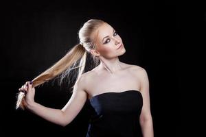 Beauty fashion model girl with long healthy smooth straight hair ponytail hairstyle on black background. Smiling pretty woman looking camera. Perfect Fresh Skin Portrait. Youth and Skin Care Concept. photo