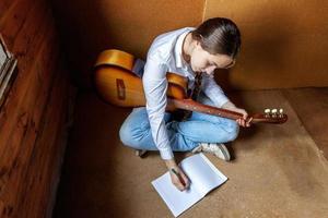 Young hipster woman sitting on floor and playing guitar at home. Teen girl learning to play song and writing music in her room. Hobby, lifestyle, relax, Instrument, leisure, education concept. photo