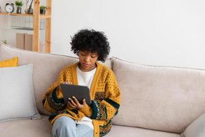 African american girl holding digital tablet touch screen typing scroll page at home. Woman with mobile tech device surfing internet using social media apps playing game. Study work shopping online. photo