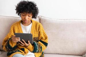 African american girl holding digital tablet touch screen typing scroll page at home. Woman with mobile tech device surfing internet using social media apps playing game. Study work shopping online. photo