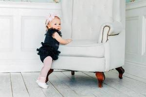 Little baby girl standing near chair in bright light living room smiling and laughing photo