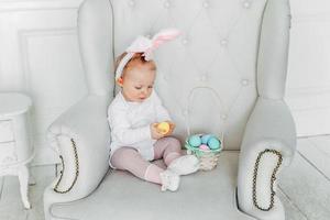 Little child girl wearing bunny ears on Easter day and playing with painted eggs photo