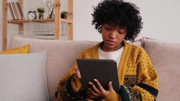 African american girl holding digital tablet touch screen typing scroll page at home. Woman with mobile tech device surfing internet using social media apps playing game. Study work shopping online. photo