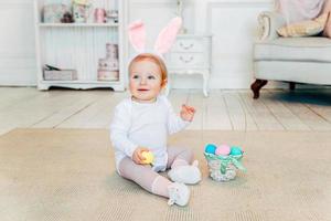 Little child girl wearing bunny ears on Easter day and playing with painted eggs photo