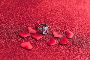 Will you marry me. Wedding ring and many red hearts on red glitter background. Engagement marriage proposal wedding concept. St. Valentine's Day postcard. Banner on valentines day. photo
