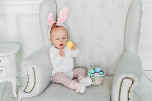 Little child girl wearing bunny ears on Easter day and playing with painted eggs photo