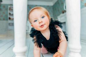 Little crawling baby girl one year old siting on floor in bright light living room smiling and laughing photo