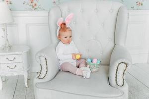 Little child girl wearing bunny ears on Easter day and playing with painted eggs photo