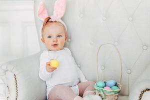 Little child girl wearing bunny ears on Easter day and playing with painted eggs photo