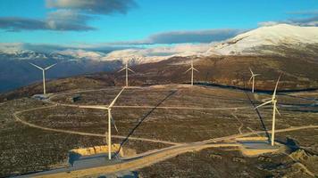 molinos de viento en las colinas durante la puesta de sol. energía renovable, energía verde. montañas en el fondo con nieve. energía eólica y respetuoso con el medio ambiente. Futuro sostenible. acabar con los combustibles fósiles.