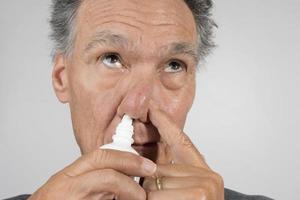 Senior man using a Nasal Spray for his dry nose photo