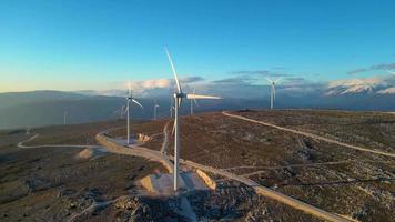 väderkvarnar på de kullar under solnedgång. förnybar energi, grön energi. bergen i de bakgrund med snö. vind kraft och miljömässigt vänlig. hållbar framtida. slutet fossil bränslen. video