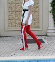 modelo con un vestido blanco y botas altas de cuero rojo está tomando una foto