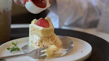 Woman taking a bite of strawberry shortcake with fork. Close Up person eating cutting yummy delicious piece of white cake topping fresh strawberry with fork on the table at cafe. Fruit cake on plate. video