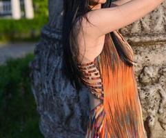 hermosa modelo morena con cabello largo está tomando una foto en el parque. la mujer lleva un vestido largo de verano naranja