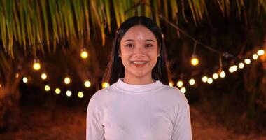 Footage of an Asian young happy man looking at camera and smiling with light bokeh background. Party and celebration concept. Slow motion. video