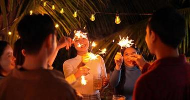 imágenes de un feliz grupo asiático de amigos divirtiéndose con bengalas al aire libre - jóvenes divirtiéndose con fuegos artificiales por la noche - gente, comida, estilo de vida de bebida, concepto de celebración de año nuevo.