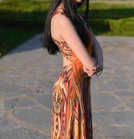 hermosa modelo con cabello largo está tomando una foto en el parque. la mujer lleva un vestido largo de verano naranja