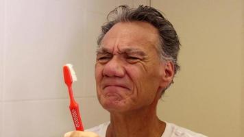 homem sênior olhando para sua velha e desgastada escova de dentes video