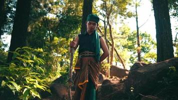 An Asian man in green clothes holding a stick while walking lonely in the forest and enjoying the view video