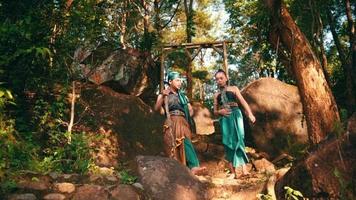 Asian couple walking down the hill above the mountain with a forest in the background while chatting together in green clothes video