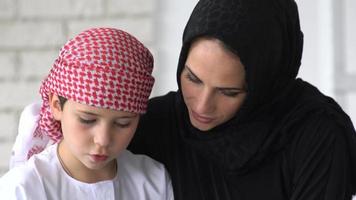 Lycklig arabicum mor och son tillsammans Sammanträde på de soffa och läsning en bok. video