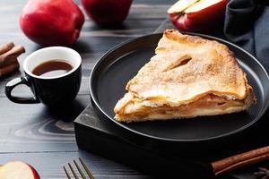 trozo casero de tarta de manzana con manzanas rojas frescas sobre mesa negra foto