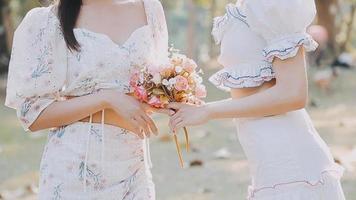 Young pretty brunette twin girls sitting on the grass with legs slightly bent in knees and looking in a brown book, wearing casual coat in autumn sunny weather on blurry background. video