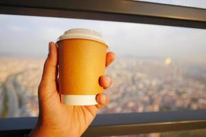 hand holding take away paper cup against city background photo
