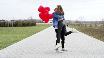 Liebe. Junger Mann umarmt und küsst ein Mädchen im Park mit roten Luftballons video