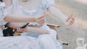 Young pretty brunette twin girls sitting on the grass with legs slightly bent in knees and looking in a brown book, wearing casual coat in autumn sunny weather on blurry background. video