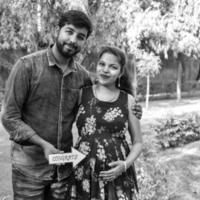 Indian couple posing for maternity baby shoot. The couple is posing in a lawn with green grass and the woman is falunting her baby bump in Lodhi Garden in New Delhi, India photo