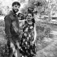 Indian couple posing for maternity baby shoot. The couple is posing in a lawn with green grass and the woman is falunting her baby bump in Lodhi Garden in New Delhi, India photo