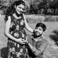 Indian couple posing for maternity baby shoot. The couple is posing in a lawn with green grass and the woman is falunting her baby bump in Lodhi Garden in New Delhi, India photo