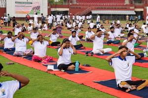 New Delhi, India, June 21 2022 - Group Yoga exercise session for people at Yamuna Sports Complex in Delhi on International Yoga Day, Big group of adults attending yoga class in cricket stadium photo