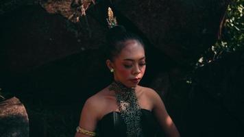 Asian woman in traditional green dress meditating lonely in peacefully in front of the big rock at the mountain video