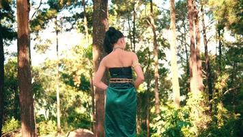 uma mulher asiática jogando seus longos cabelos negros em pé na floresta com um vestido verde video