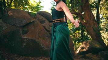 An Asian woman with a traditional dance costume dances near the big rock beautifully with brown leaves in the background video