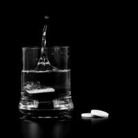 An effervescent tablet falls into a glass beaker on a black background photo